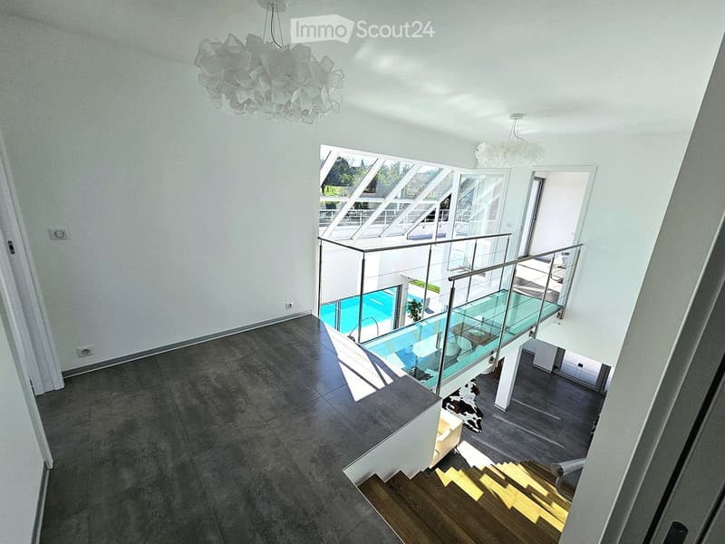 Modern hallway with a glass staircase leading to a pool area below, featuring contemporary lighting and sleek design.