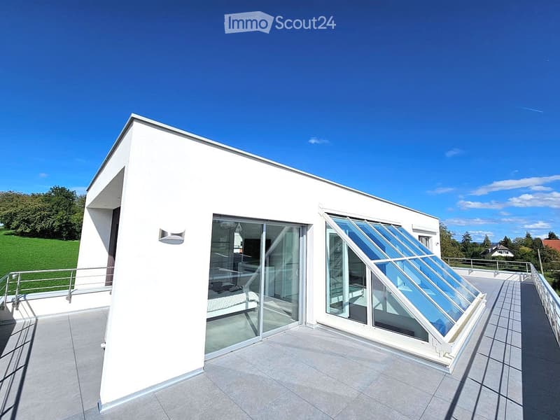 Modern white building with a large, open terrace featuring glass sliding doors and a retractable roof section.