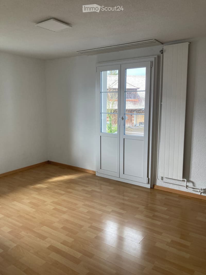 Empty room with wooden flooring, white walls, and a large white sliding door leading to an outdoor area.