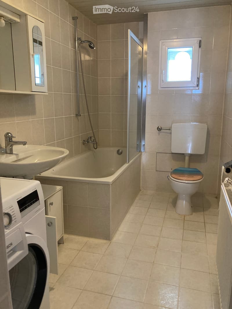 Bathroom with beige tiles, toilet, bathtub, sink, mirror, and washing machine.
