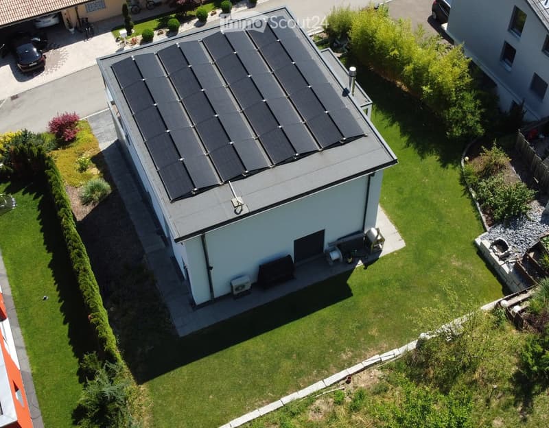 Aerial view of a modern house with solar panels on the roof, surrounded by a well-maintained lawn and garden area.