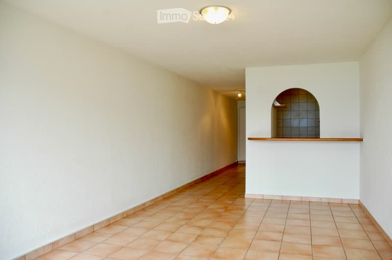 Empty hallway with tiled floor, white walls, and recessed lighting. Features an arched opening leading to another area.