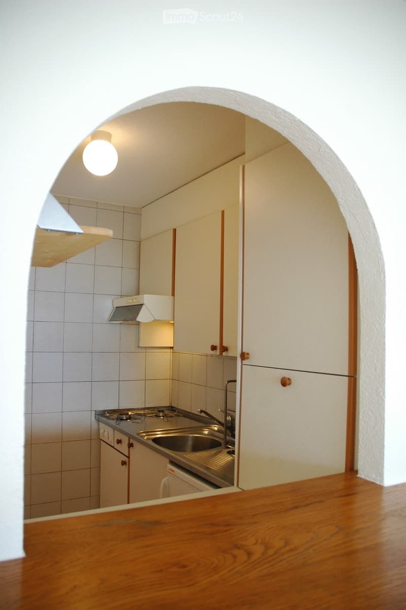 Compact kitchen with white tiled walls, stainless steel sink, stove, and fitted cabinets.