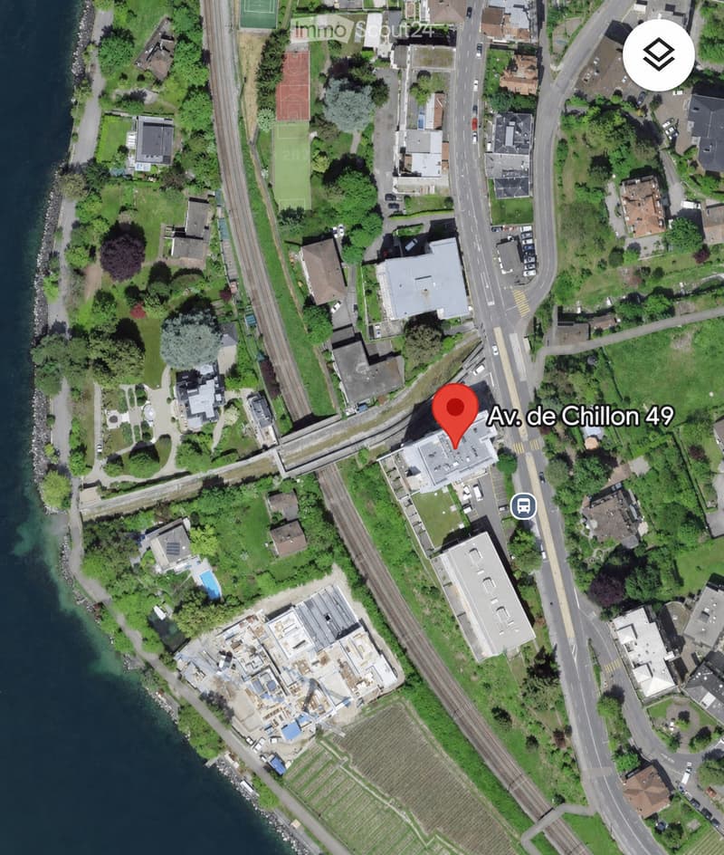 Aerial view of a residential area with multiple houses, green spaces, a railway line, and a waterfront area with a swimming pool visible.