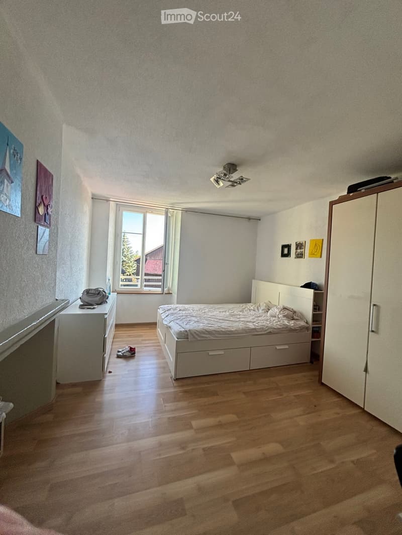Bedroom with wooden flooring, a bed with a headboard, a wardrobe, a nightstand, and several picture frames on the walls.
