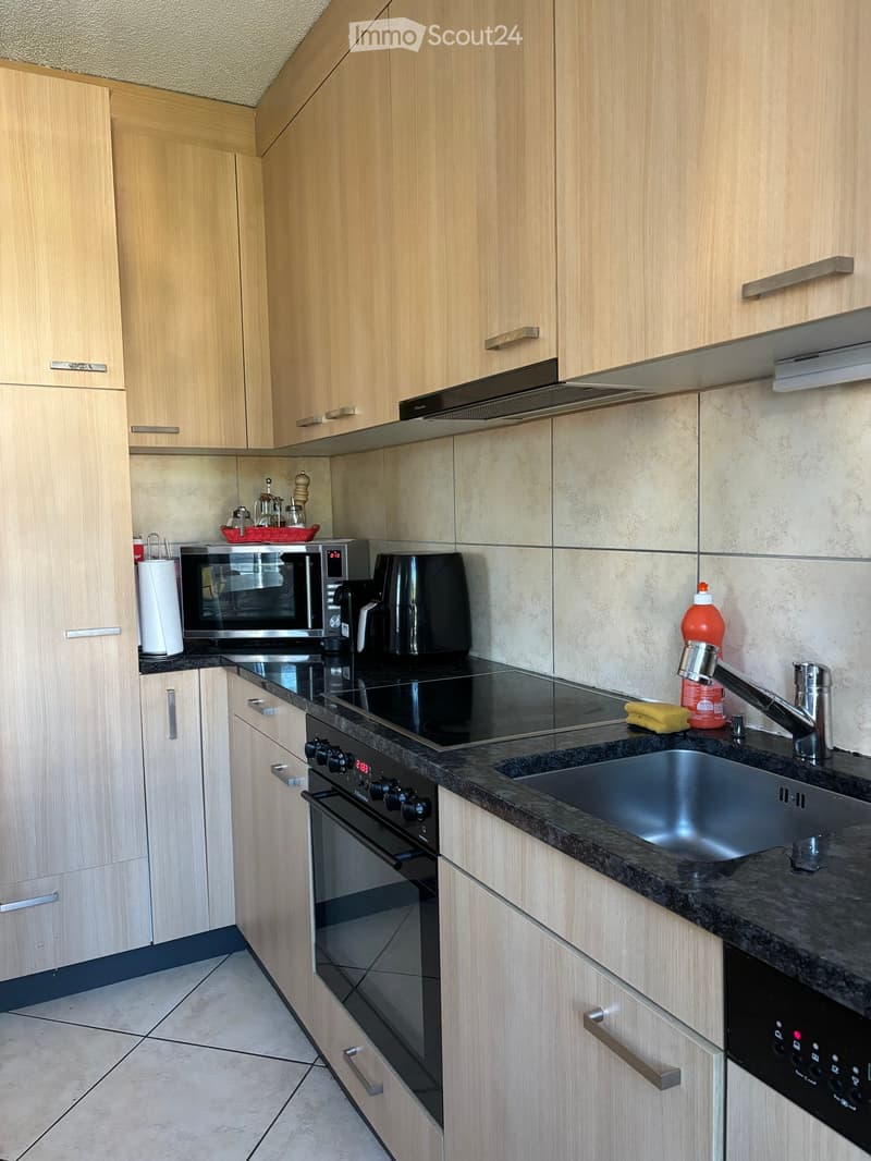 Modern kitchen with light wood cabinets, stainless steel appliances, granite countertops, and a built-in oven and microwave.