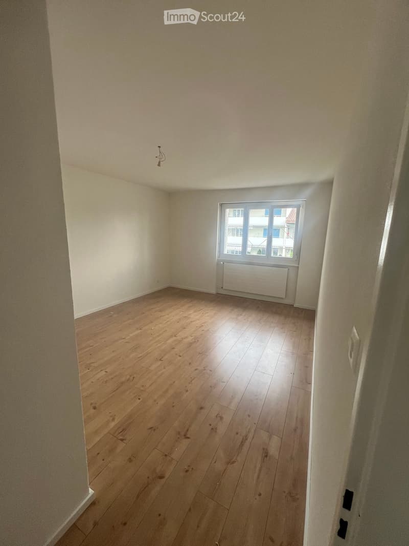 Empty room with wooden flooring, white walls, and a window with a radiator below it.