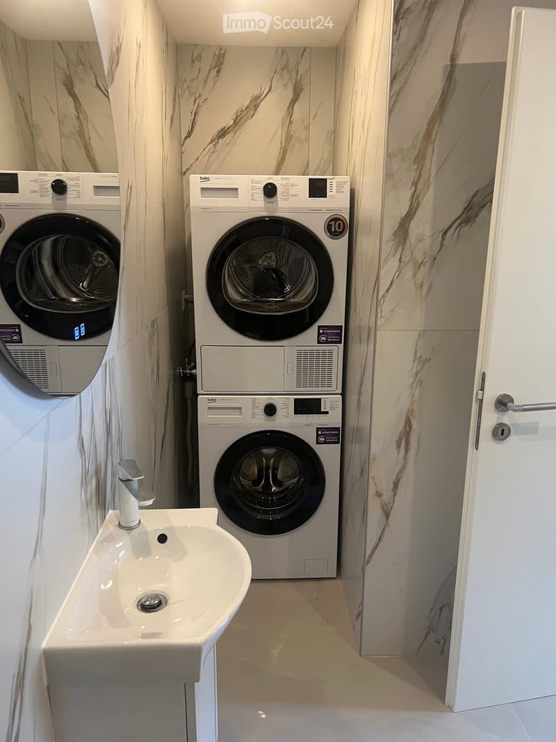 Modern bathroom with marble walls, a white sink with a chrome faucet, and two stacked washing machines.