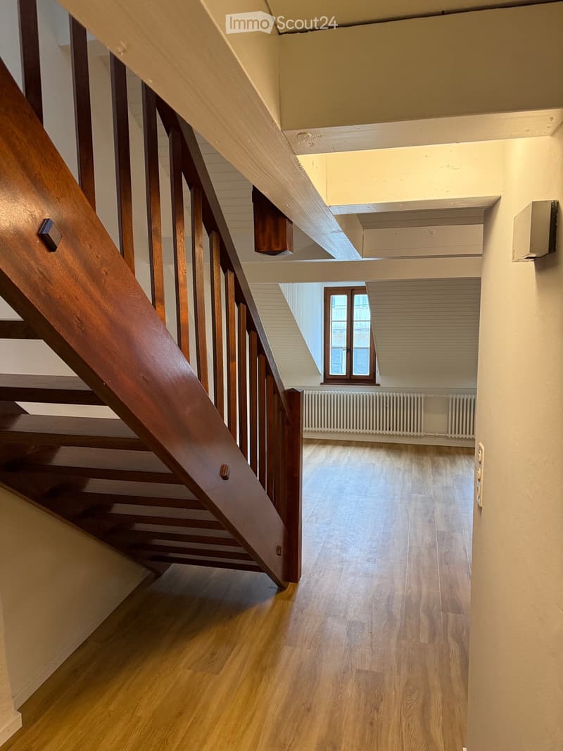 Wooden staircase with wooden railings and a wooden floor, leading to a room with a window and radiator.