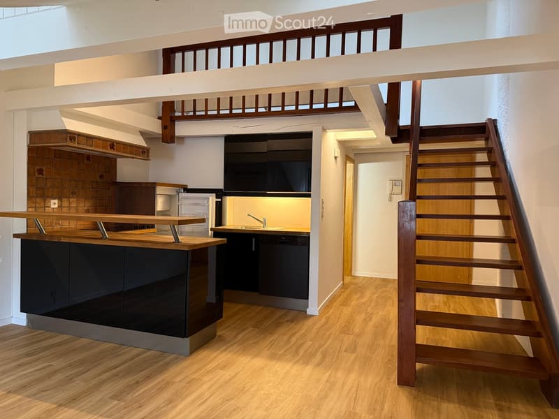 Modern kitchen with wooden flooring, black cabinets, a kitchen island, and a staircase leading to an upper level.