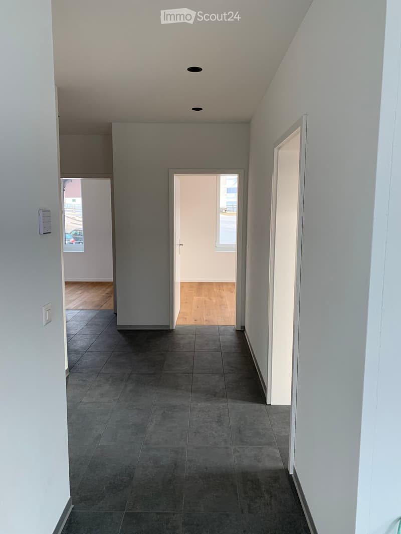 Empty hallway with grey tiled floor, white walls, and multiple doors leading to other rooms.