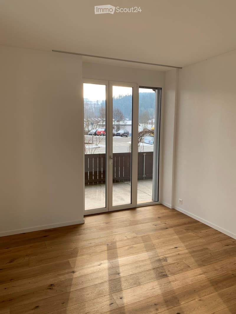 Empty room with light wooden flooring and large sliding glass doors leading to an outdoor area.