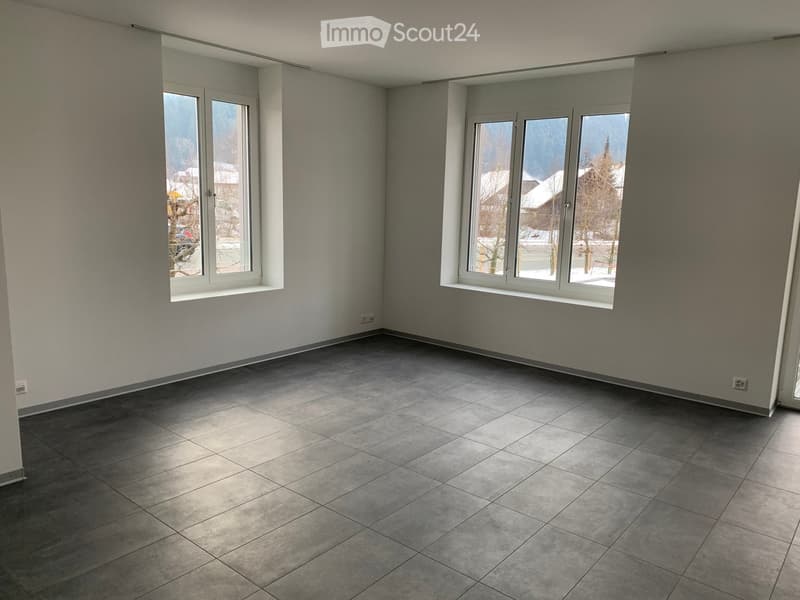 Empty room with grey tiled floor, white walls, and large windows offering a view of a snowy landscape.