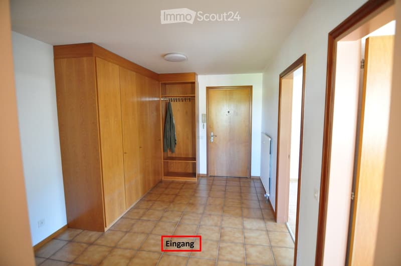 Empty hallway with tiled floor, wooden doors, built-in wooden closet, and coat hanging on the closet door.