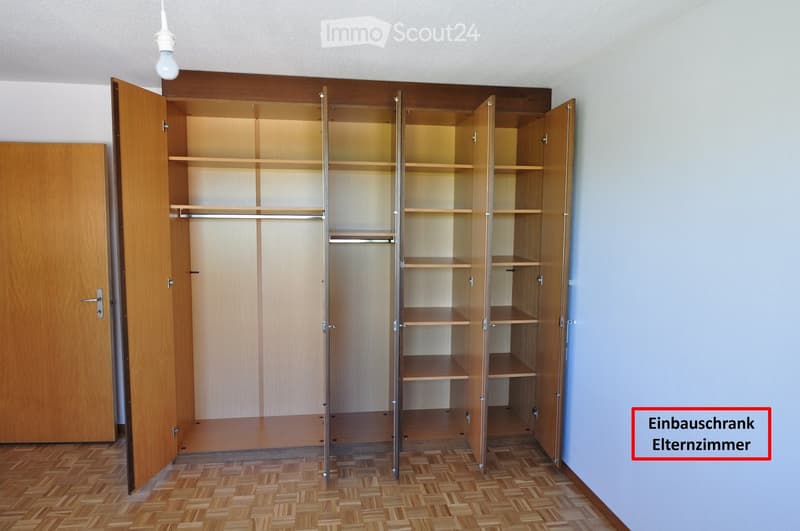 Empty room with wooden floor, built-in wardrobe with open doors and shelves, and a hanging light fixture.