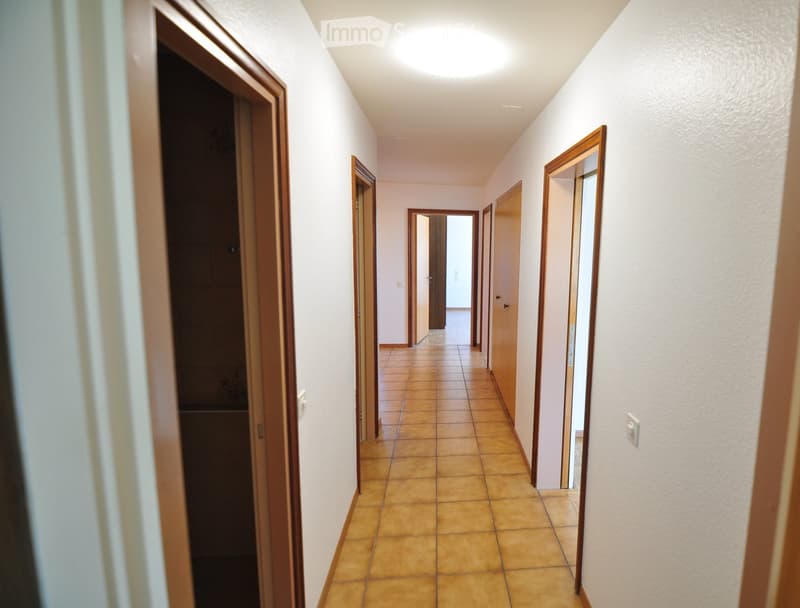 Empty hallway with tiled floor, wooden doors, and light-colored walls.
