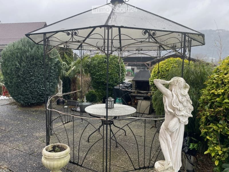 Outdoor patio area with a metal gazebo, round table, chairs, potted plants, and a decorative statue.