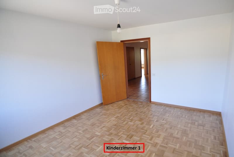 Empty room with light blue walls, wooden herringbone flooring, and a single open wooden door leading to another room.