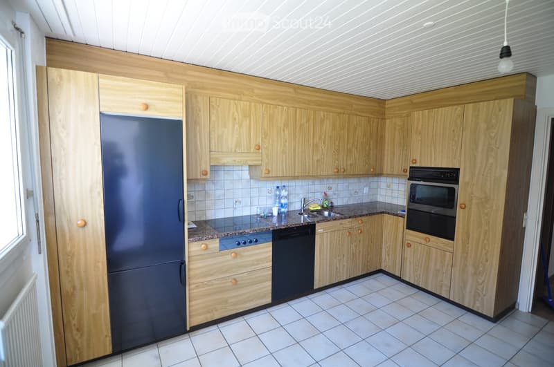 Modern kitchen with light wooden cabinets, stainless steel appliances, and tiled flooring.