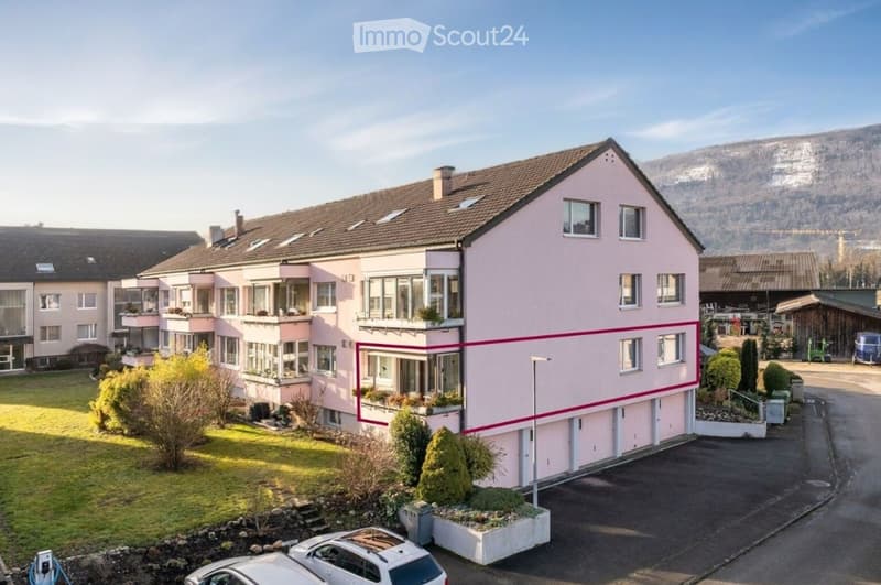 Two-story pink house with multiple windows, garage, and surrounding greenery.