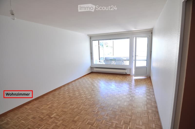 Empty room with wooden herringbone flooring, white walls, large window with a view, and a radiator below the window. No furniture or personal items are present.