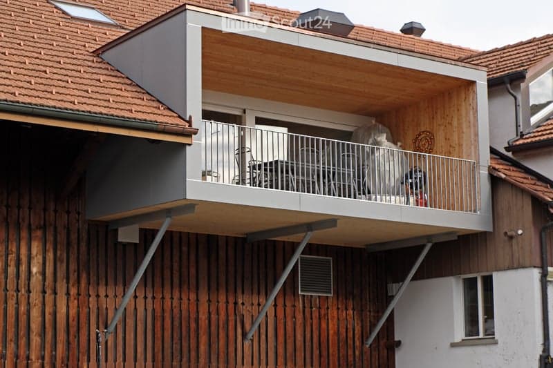 Balcony with wooden decking, metal railing, and outdoor furniture including a table and chairs.