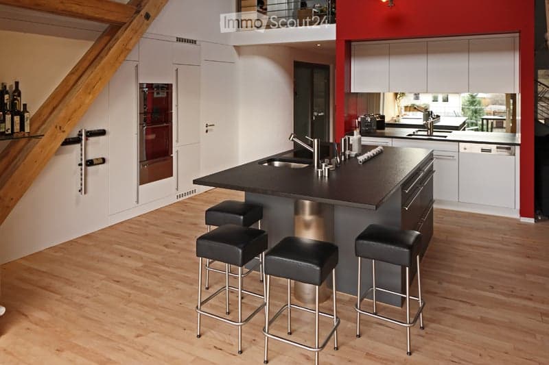 Modern kitchen with a central island, four black stools, white cabinets, and a stainless steel sink.