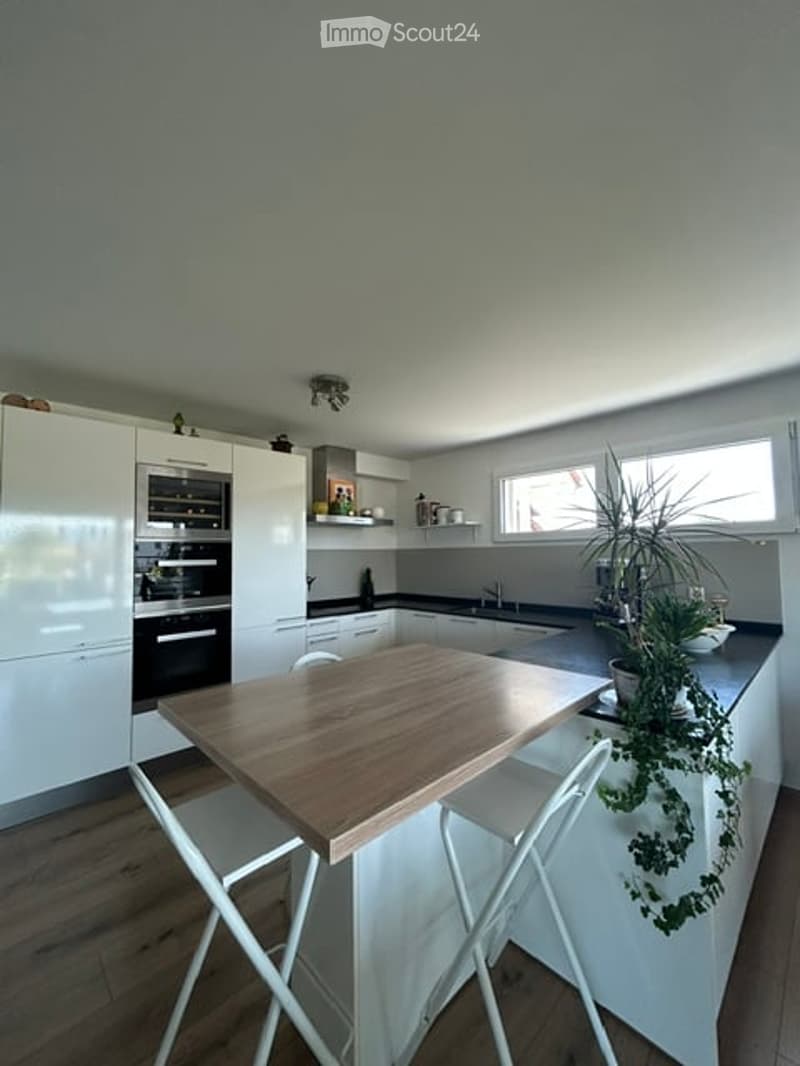Modern kitchen with white cabinets, black oven, wooden table, white chairs, and a potted plant on the counter.