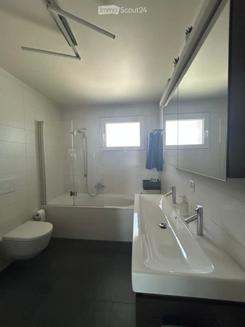 Modern bathroom with white tiles, a bathtub, toilet, sink, mirror, and a shower area with a glass enclosure.