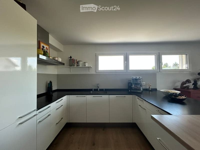 Modern kitchen with white cabinets, black countertops, and wooden flooring. Features include a sink, faucet, coffee maker, bowl, and a framed picture on the shelf.