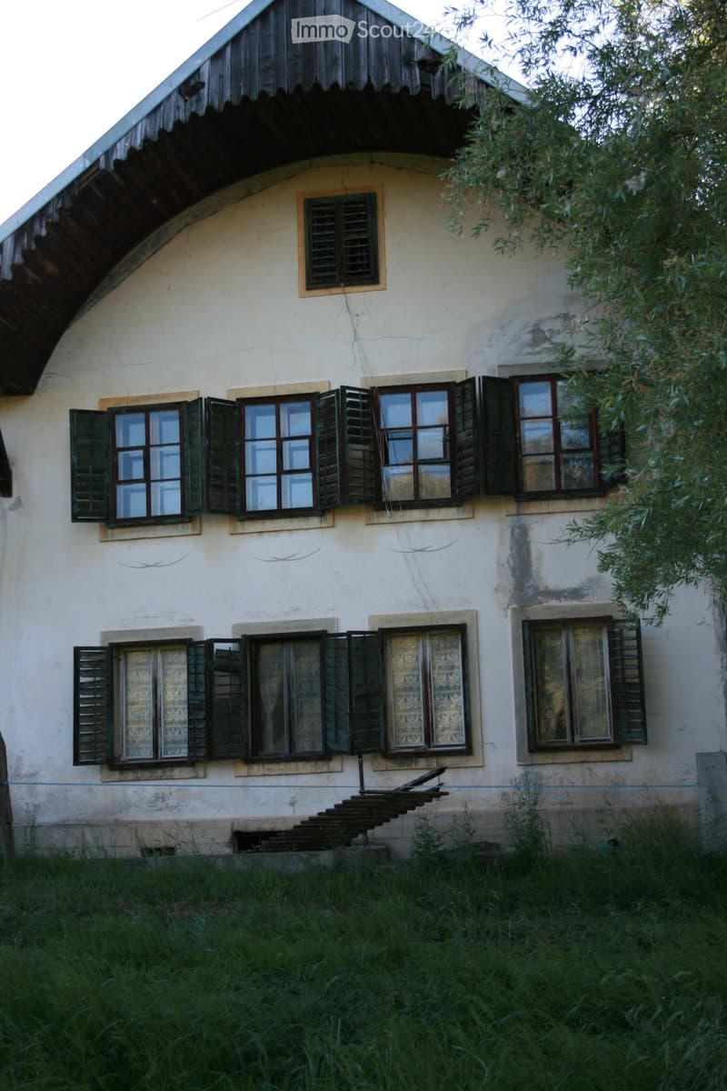 Two-story house with white exterior, multiple windows with shutters, and a small staircase leading to the entrance.