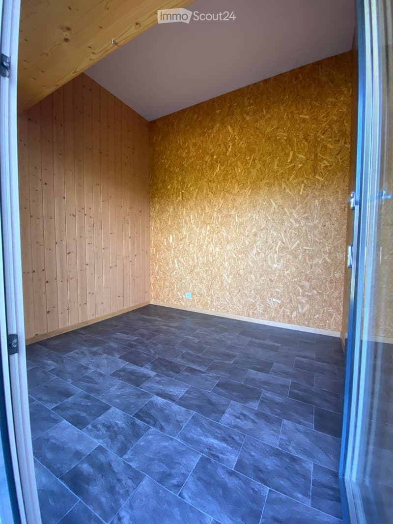 Empty room with wooden walls, dark grey tiled floor, and a partially visible door frame on the left side.