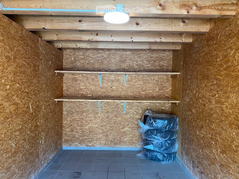Empty room with wooden walls, shelves, and a light fixture on the ceiling. The floor is tiled, and there are plastic bags in the corner.