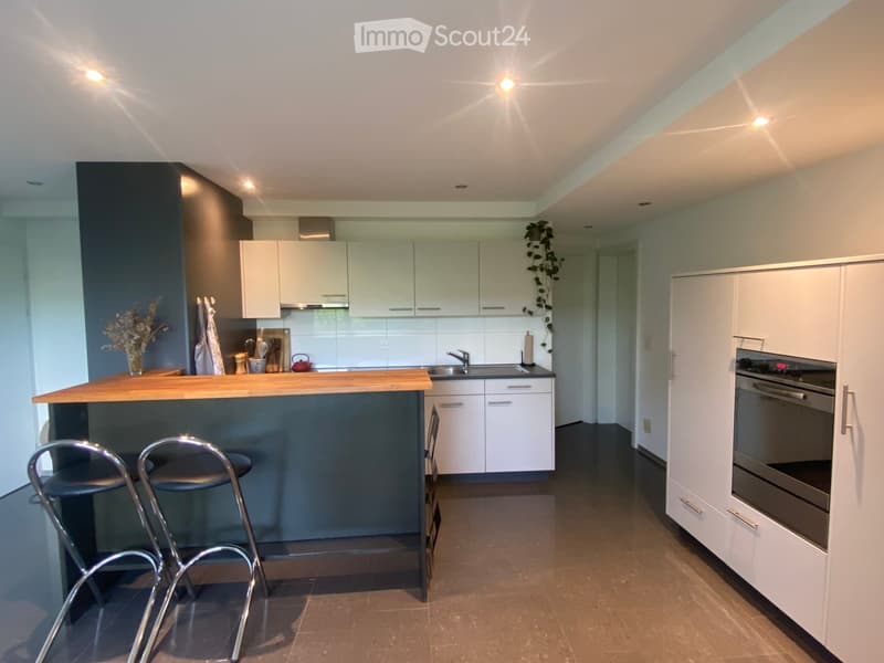 Modern kitchen with white cabinets, wooden countertop, bar stools, and stainless steel appliances including an oven and sink.