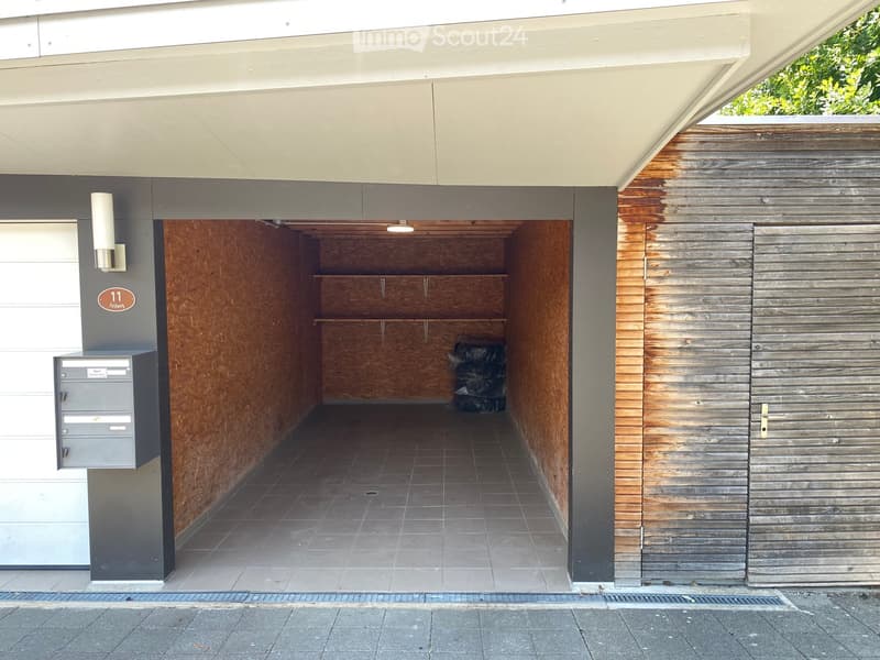 Modern covered parking area with wooden shelving, tiled floor, and a grey mailbox unit on the left side.