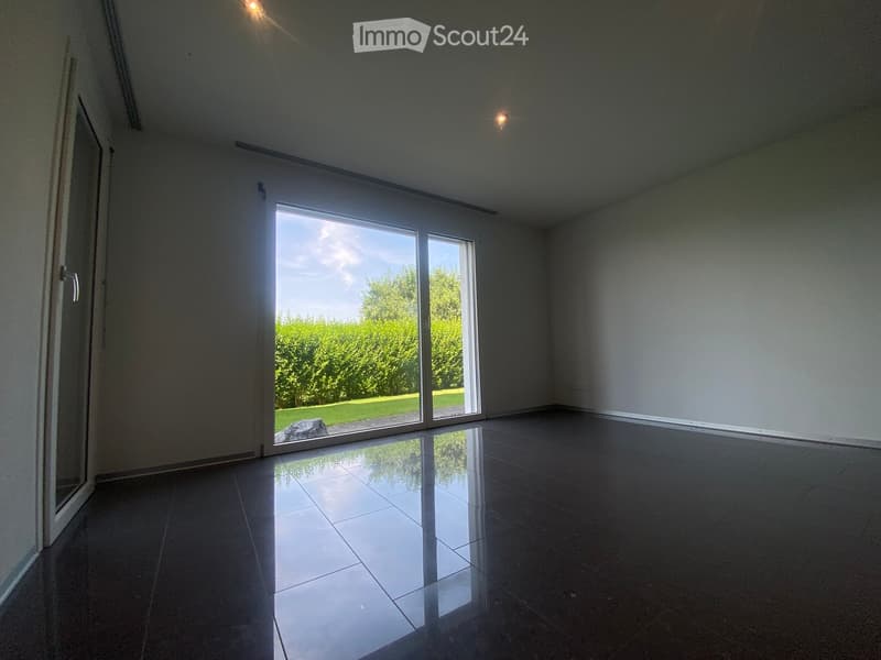 Empty room with large sliding glass doors leading to a garden, polished tile floor, and recessed lighting.