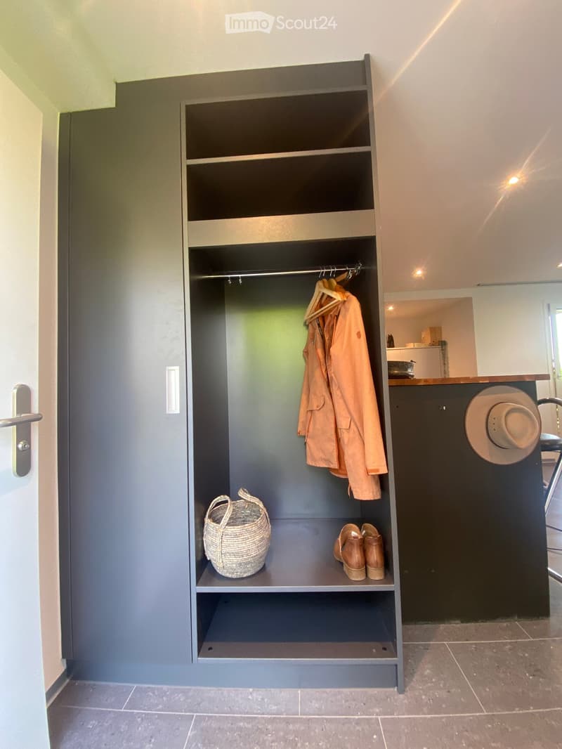 A modern, well-organized closet with built-in shelving and a hanging rod. Contains a coat, a hat, a woven basket, and a pair of shoes.