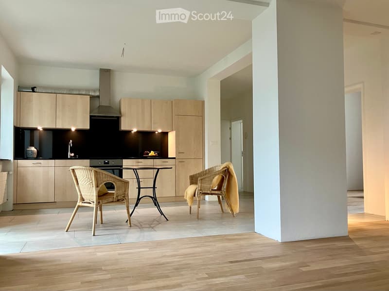 Modern kitchen with light wooden cabinets, stainless steel appliances, and a small dining area with wicker chairs and a round table.