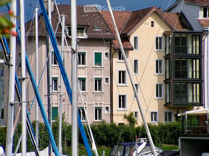 Multi-story residential building with beige and cream facades, multiple windows, and a balcony on the right side.