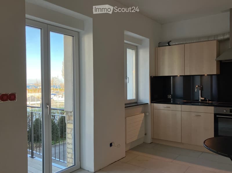 Modern kitchen with light wood cabinets, stainless steel appliances, and a large sliding glass door leading to a balcony.