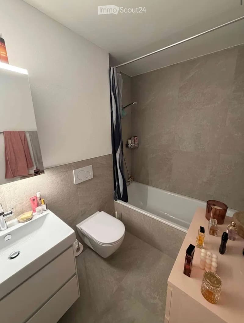 Modern bathroom with a sink, toilet, bathtub, and mirror. Cosmetic items and candles are placed on the vanity.
