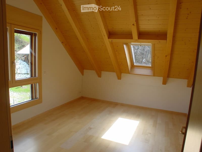 Empty attic room with wooden beams, light wooden flooring, and large windows allowing natural light to enter.