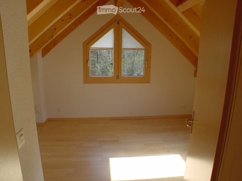 Empty attic room with wooden floors, exposed wooden beams, and a skylight window offering natural light.