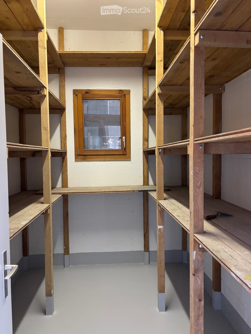 Empty room with wooden shelving units, white walls, and a single window with wooden frame.