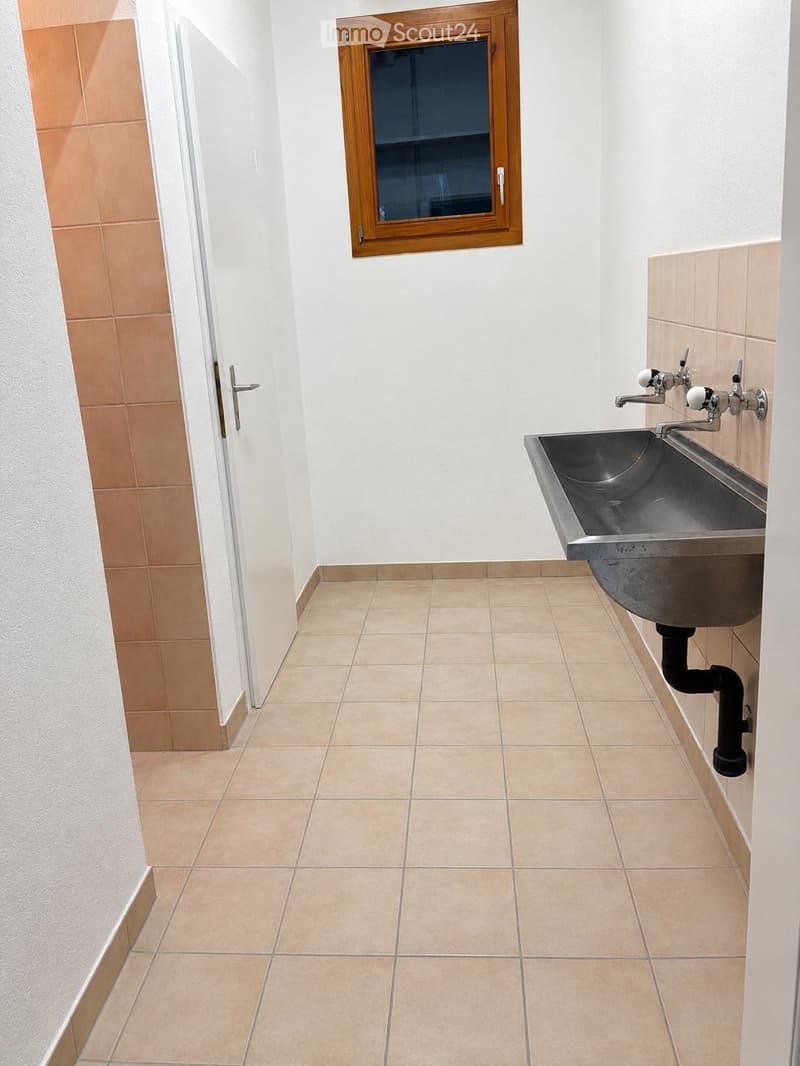 Empty bathroom with tiled floor and walls, a single sink with faucet, and a small window above it.