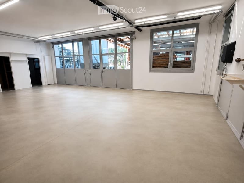 Empty room with white walls, large industrial-style windows, and a concrete floor. No furniture or equipment is present.