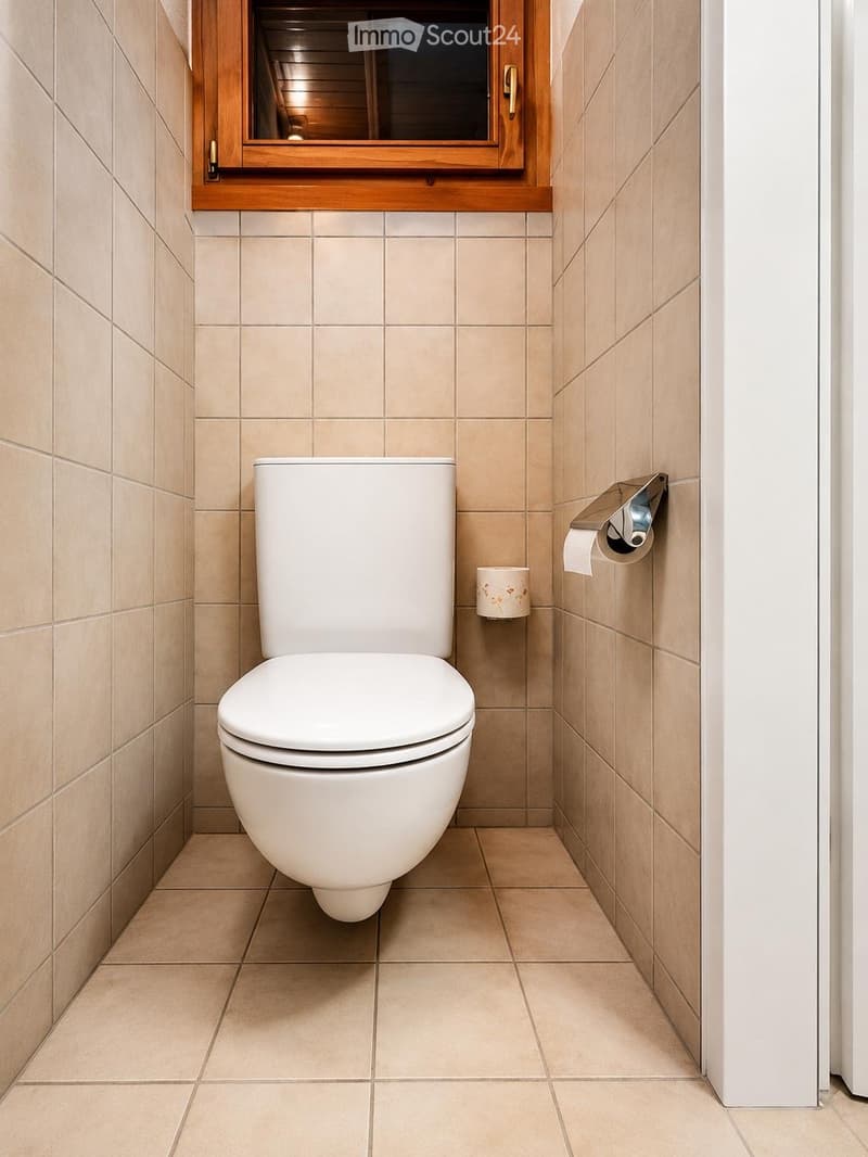 Modern bathroom with beige tiled walls and floor, white toilet, toilet paper holder, and a small window with wooden frame above the toilet.