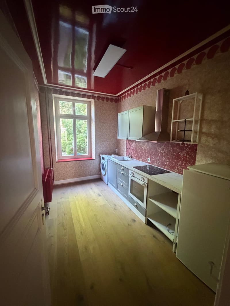 Kitchen with wooden flooring, white cabinets, sink, oven, washing machine, and radiator.