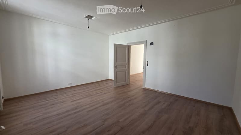 Empty room with wooden flooring, white walls, and two doors leading to adjacent spaces.