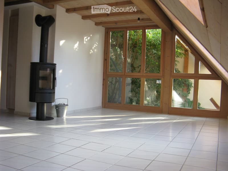 Bright, empty room with white tiled flooring, large wooden-framed windows, and a modern black wood-burning stove.